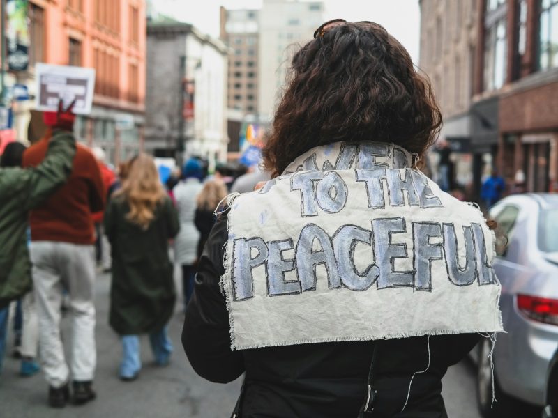 Une manifestante de dos porte une pancarte en tissu « Power to the Peaceful » lors d’une marche